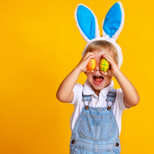 funny happy child boy with easter eggs and bunny ears on yellow background