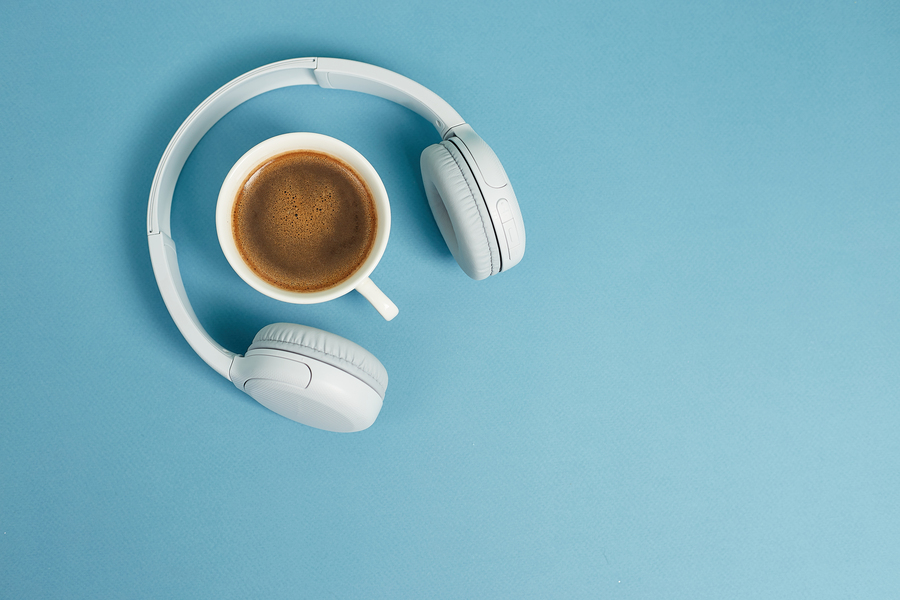 Café e fones de ouvido sob uma mesa azul: podcast sobre negócios