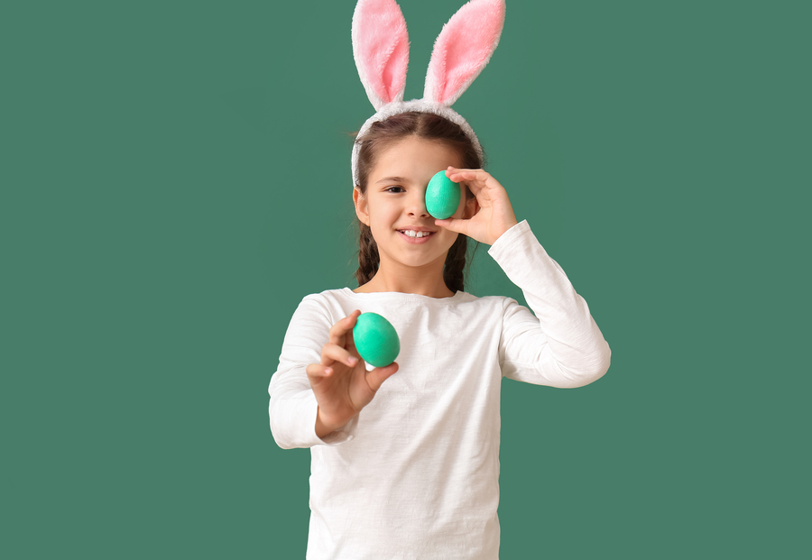 Funny little girl with bunny ears and Easter eggs on green background