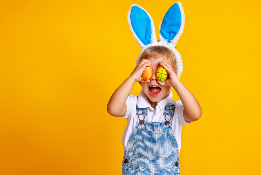 funny happy child boy with easter eggs and bunny ears on yellow background