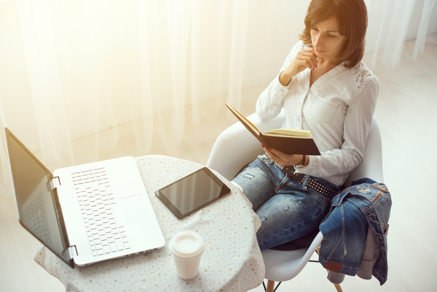 Empresária lendo sobre tipos de franquia num livro perto de uma mesa com notebook e café. 